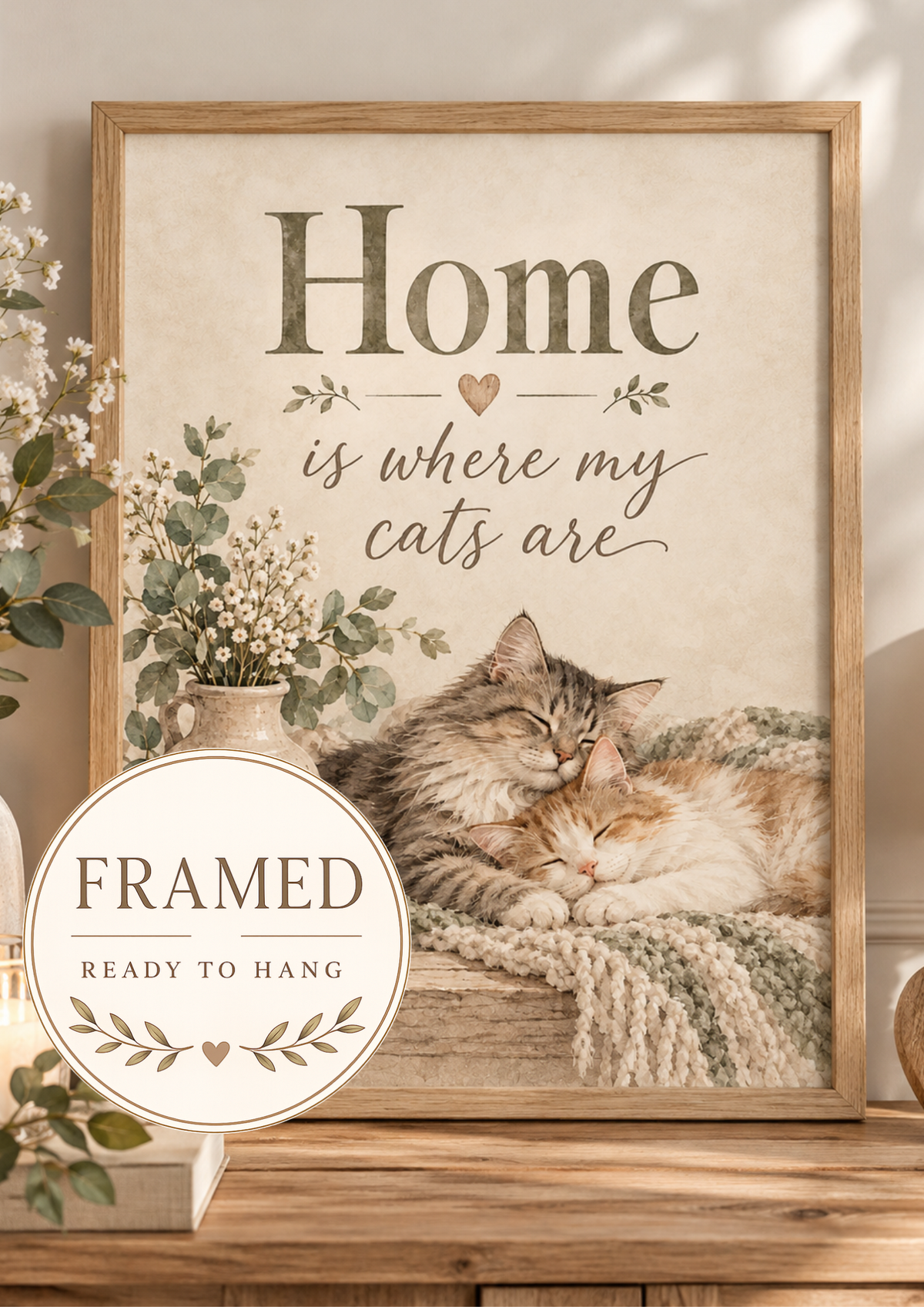 Home is where my cats are artwork with two sleeping cats, white flowers, sage foliage, candle, wooden heart and knitted blanket; framed and ready to hang badge