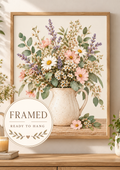 Pink wildflowers and white daisies with lavender stems and green foliage in a cream ceramic jug on a rustic tabletop; framed and ready to hang badge