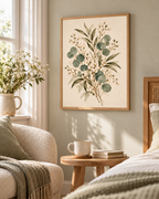 Delicate sage green eucalyptus, olive-toned foliage and ivory-white flowers on a warm neutral background styled in a reading corner