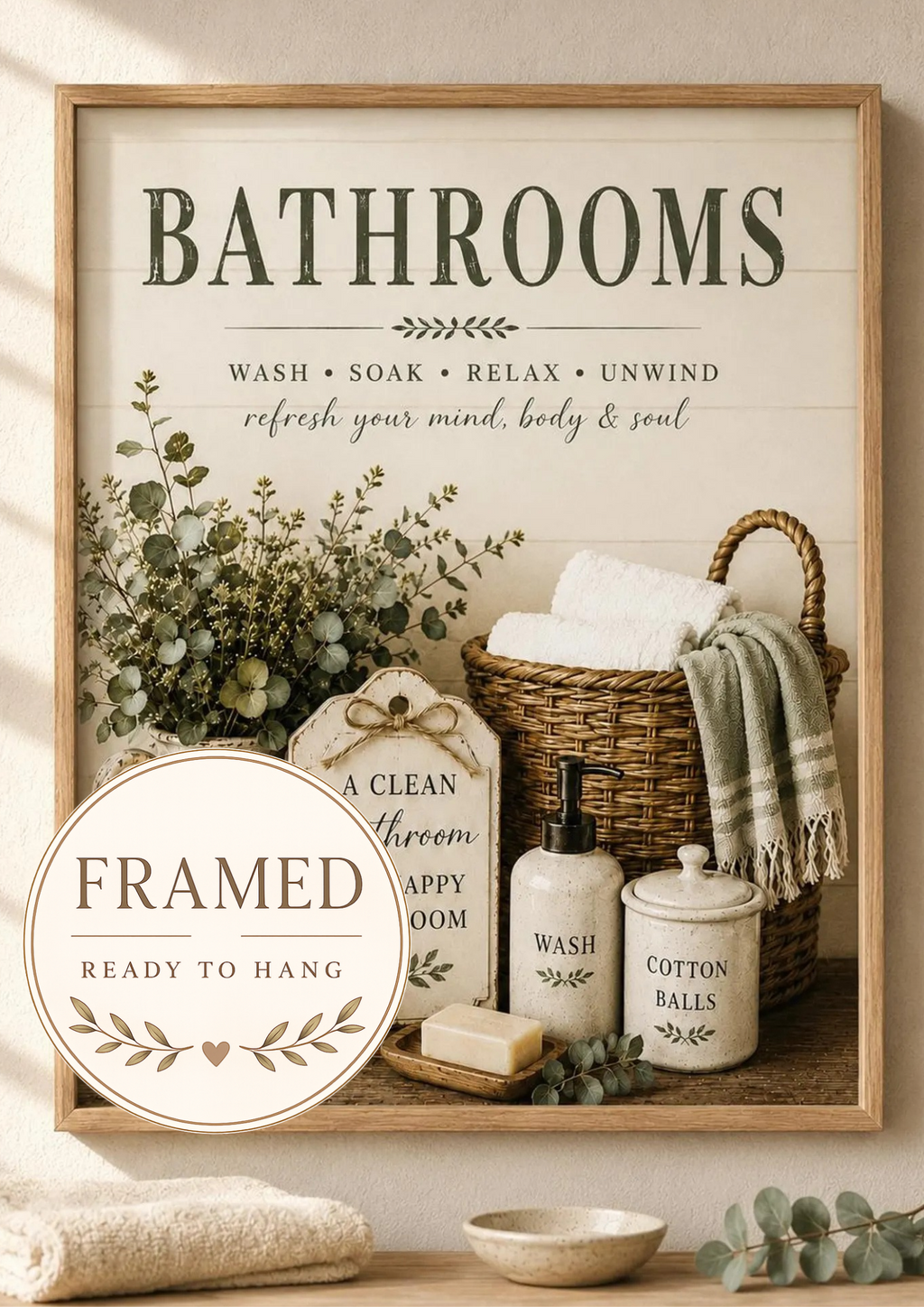 Farmhouse bathroom typography with wash soak relax unwind wording, sage foliage, towels, wicker basket and ceramic accessories; framed and ready to hang badge
