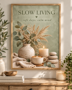 Slow Living artwork with sage green foliage, dried grasses, a coffee cup, candle, ceramic vase and pebbles; print only, frame not included