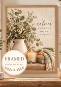 A calmer happier home botanical artwork with eucalyptus, white wildflowers, rustic jug, candle, wooden house and knitted blanket; framed and ready to hang badge
