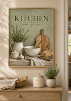 Sage green Kitchen gather cook enjoy artwork with herbs, ceramic jug, mixing bowl, wooden utensils, bread and garlic styled in a kitchen console display