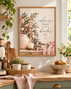 A calmer mind creates a kinder life quote with pink and ivory flowers, sage foliage, ceramic vase, candle, books and blush knitted throw styled in a kitchen