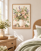 Pink wildflowers and white daisies with lavender stems and green foliage in a cream ceramic jug on a rustic tabletop styled in a bedroom