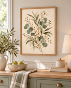 Delicate sage green eucalyptus, olive-toned foliage and ivory-white flowers on a warm neutral background styled in a kitchen
