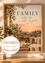 Family makes life a little brighter quote with Tuscan countryside sunset, olive greenery, white flowers, rustic ceramics and candlelight; framed and ready to hang badge