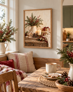 Rustic Christmas artwork with a gingerbread house, winter greenery, candle and wrapped gifts beside a cosy armchair