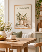 Bedroom rest reset dream quote with white flowers, sage foliage, ceramic vase, candle, books and soft neutral bedding styled in a dining room