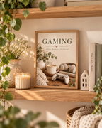 Gaming room artwork with Play Pause Recharge quote, controller, headphones, coffee and foliage in a styled home display
