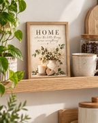 Home quote artwork styled on a wooden shelf beside plants and a mug