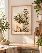 Neutral botanical artwork with white flowers, foliage, a cream vase, candle and wooden house above a sideboard